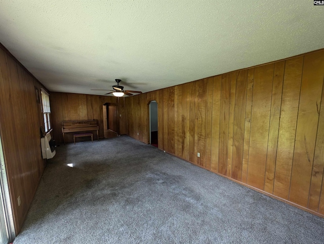 unfurnished room with carpet, ceiling fan, wood walls, and a textured ceiling