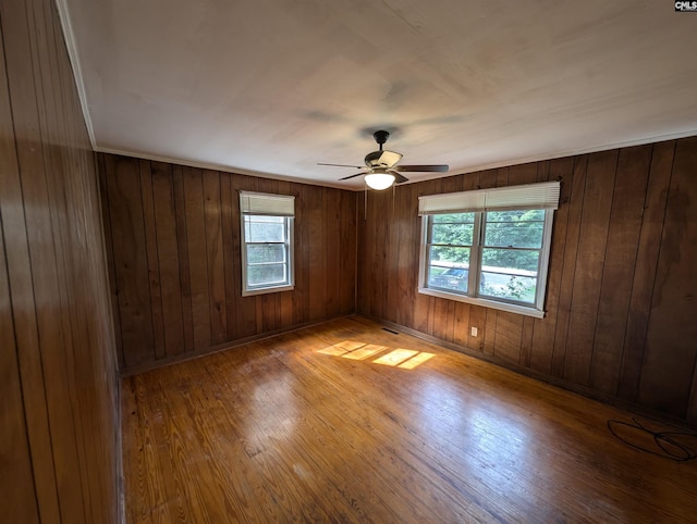 empty room with ceiling fan, wood walls, and light hardwood / wood-style flooring