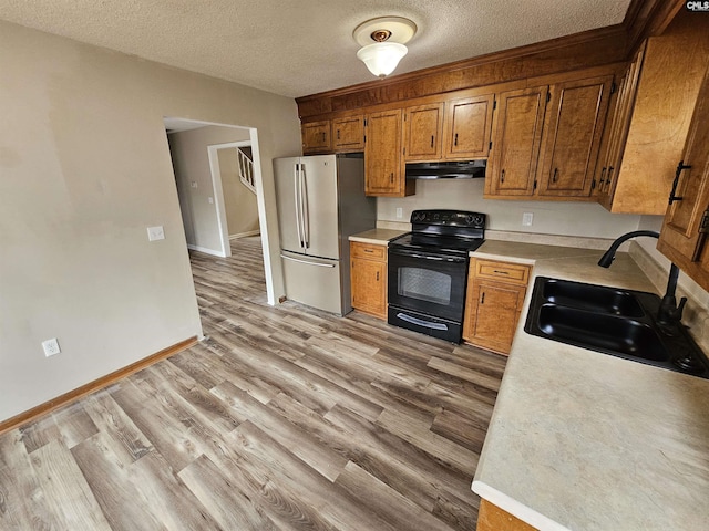 kitchen with a textured ceiling, sink, light hardwood / wood-style flooring, black range with electric stovetop, and stainless steel refrigerator