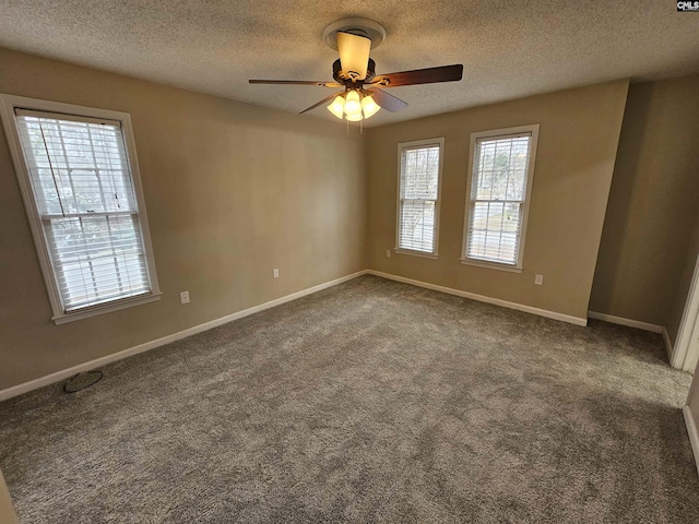 empty room featuring a healthy amount of sunlight, a textured ceiling, and dark carpet