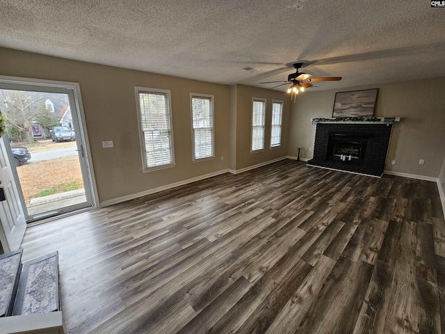 unfurnished living room featuring ceiling fan, dark wood-type flooring, a wealth of natural light, and a brick fireplace