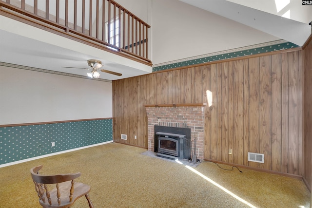 unfurnished living room featuring ceiling fan, a high ceiling, carpet, and wood walls