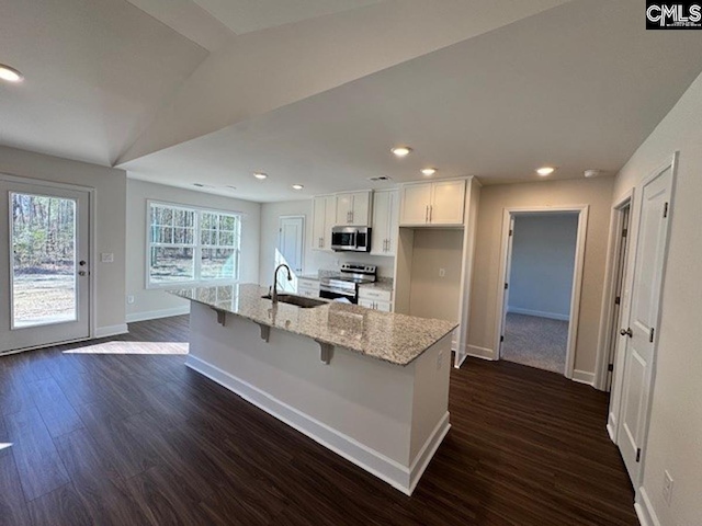 kitchen with white cabinetry, stainless steel appliances, lofted ceiling, a breakfast bar area, and a kitchen island with sink