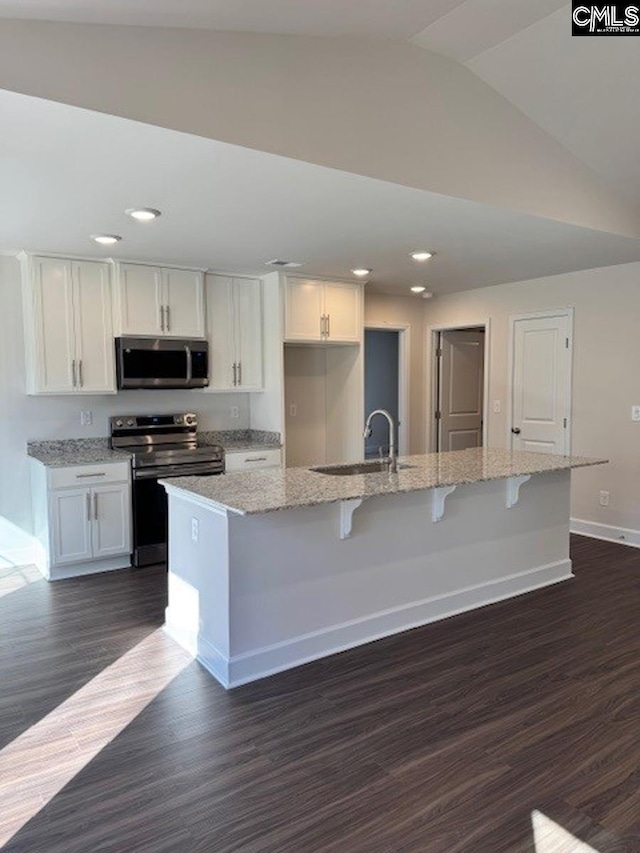 kitchen featuring vaulted ceiling, sink, white cabinetry, appliances with stainless steel finishes, and an island with sink