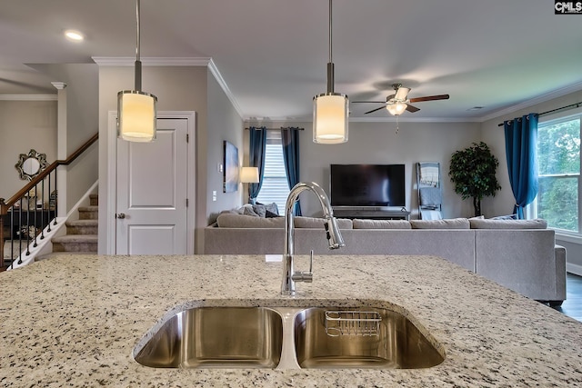 kitchen featuring decorative light fixtures, light stone counters, crown molding, and sink