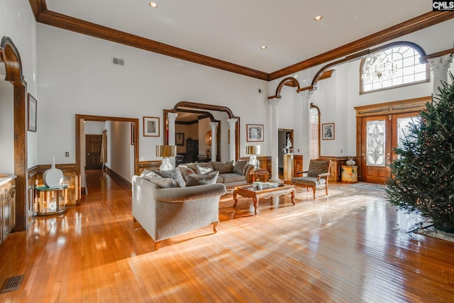 living room featuring french doors, ornamental molding, decorative columns, a towering ceiling, and light wood-type flooring