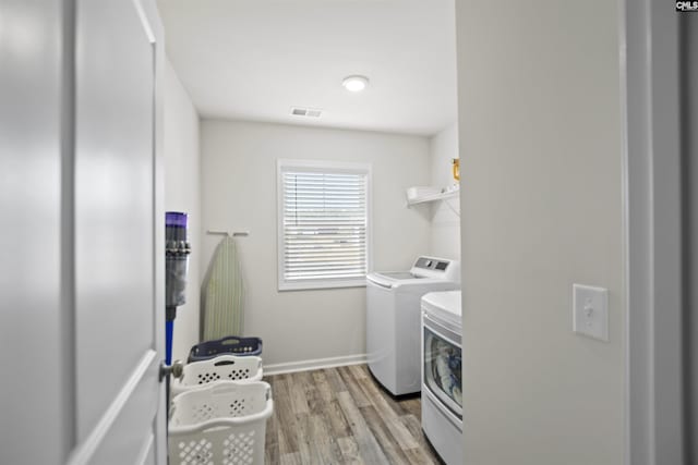 clothes washing area with washing machine and dryer and light hardwood / wood-style floors