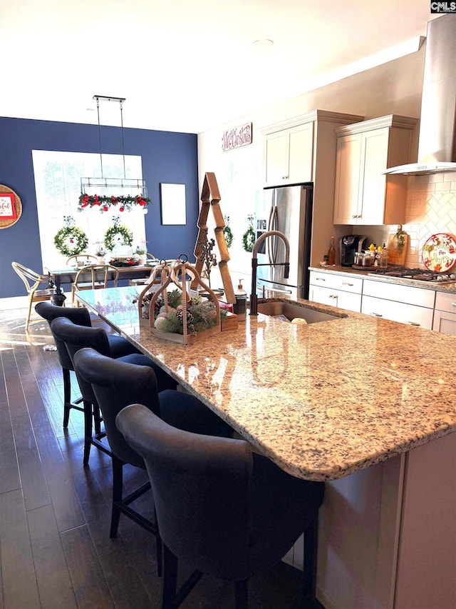 kitchen featuring decorative light fixtures, wall chimney range hood, appliances with stainless steel finishes, and a kitchen bar