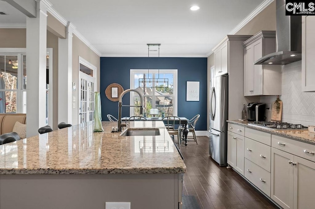 kitchen with appliances with stainless steel finishes, a large island with sink, wall chimney exhaust hood, and sink