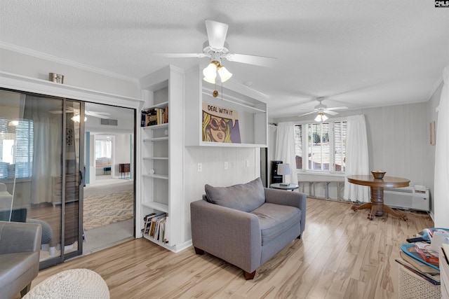 living area featuring ceiling fan, ornamental molding, a textured ceiling, and light wood-type flooring