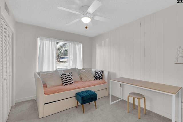 living area featuring a textured ceiling, light colored carpet, ceiling fan, and wood walls