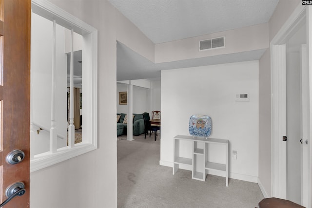 hallway featuring light colored carpet and a textured ceiling