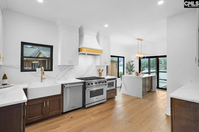 kitchen with sink, premium range hood, backsplash, pendant lighting, and appliances with stainless steel finishes