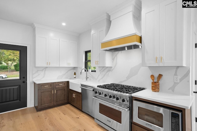 kitchen with backsplash, premium range hood, white cabinets, sink, and stainless steel appliances