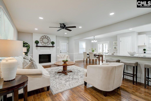 living room with a fireplace, ceiling fan with notable chandelier, and dark wood-type flooring