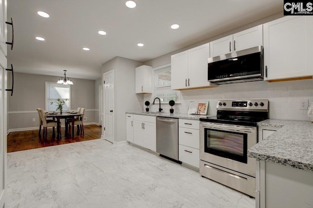 kitchen with an inviting chandelier, white cabinets, sink, light stone countertops, and appliances with stainless steel finishes