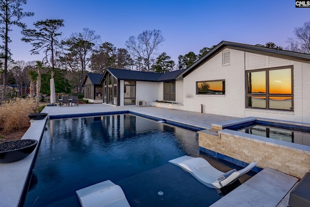 pool at dusk with an in ground hot tub and a patio