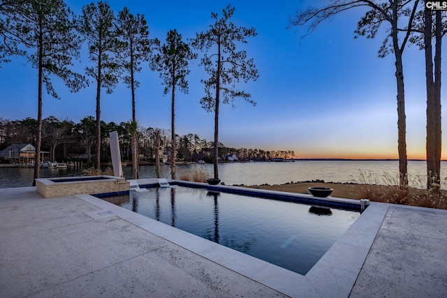 pool at dusk with an in ground hot tub and a water view