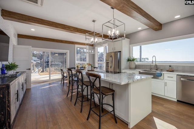 kitchen with beam ceiling, stainless steel appliances, white cabinetry, and a kitchen island