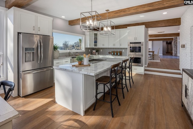 kitchen featuring a center island, hanging light fixtures, beamed ceiling, white cabinets, and appliances with stainless steel finishes