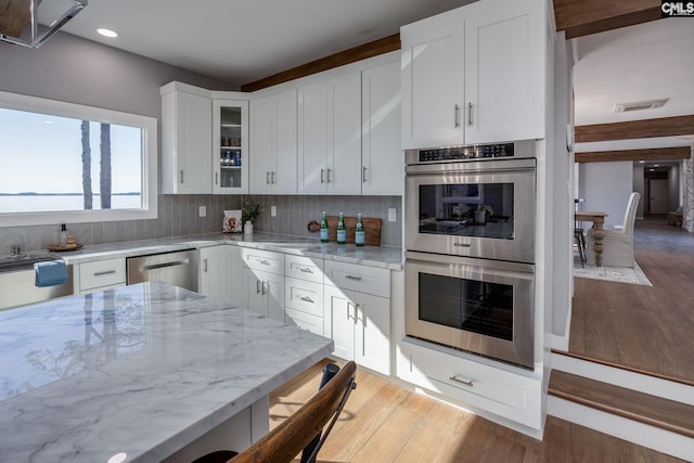 kitchen with white cabinetry, stainless steel appliances, tasteful backsplash, light stone counters, and light wood-type flooring