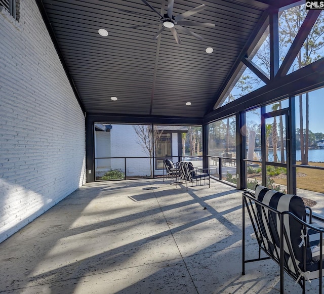 unfurnished sunroom with ceiling fan, a water view, and vaulted ceiling