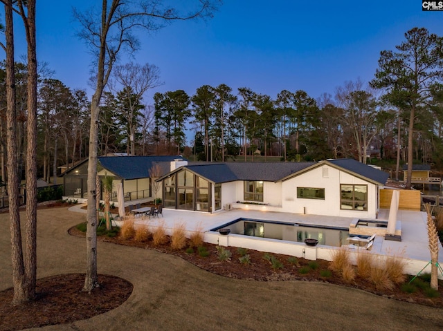 back house at dusk featuring a patio area and a sunroom