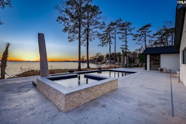 pool at dusk with a patio area, a water view, and an in ground hot tub