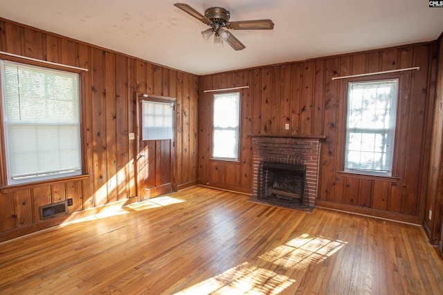 unfurnished living room featuring hardwood / wood-style floors, ceiling fan, wooden walls, and a brick fireplace