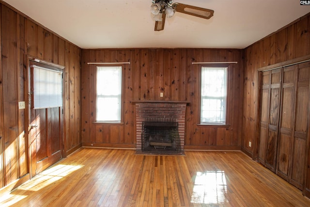 unfurnished living room featuring ceiling fan, light wood-type flooring, a wealth of natural light, and a brick fireplace