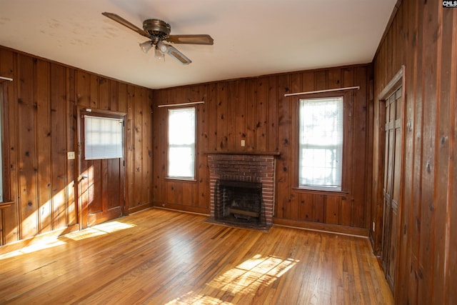 unfurnished living room featuring hardwood / wood-style floors, a brick fireplace, ceiling fan, and wood walls