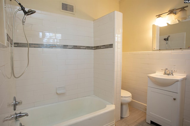 full bathroom featuring vanity, tiled shower / bath combo, toilet, tile walls, and wood-type flooring