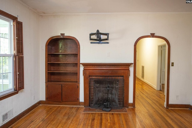 unfurnished living room featuring built in features, wood-type flooring, plenty of natural light, and ornamental molding