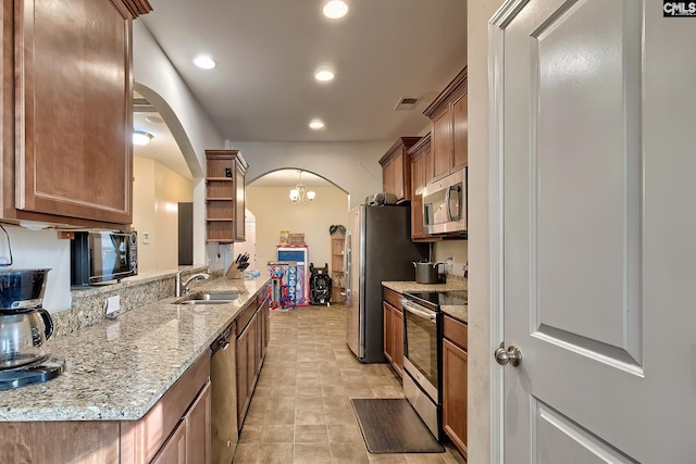 kitchen with light stone countertops, appliances with stainless steel finishes, a notable chandelier, and sink