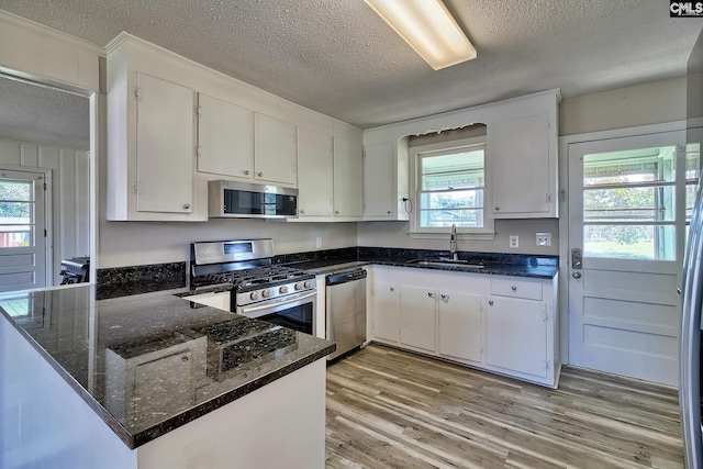 kitchen featuring kitchen peninsula, a textured ceiling, stainless steel appliances, sink, and white cabinetry