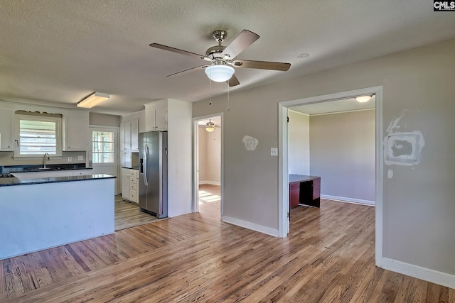 kitchen with white cabinets, stainless steel fridge, sink, and light hardwood / wood-style flooring