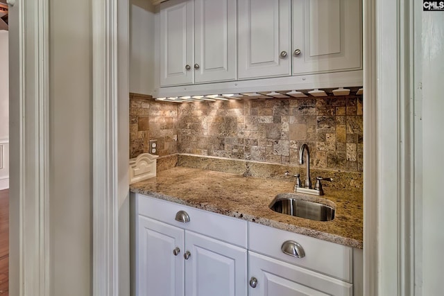 kitchen featuring tasteful backsplash, light stone countertops, sink, and white cabinets