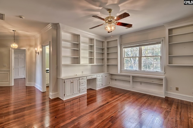 unfurnished office with ceiling fan, built in shelves, built in desk, ornamental molding, and dark hardwood / wood-style flooring