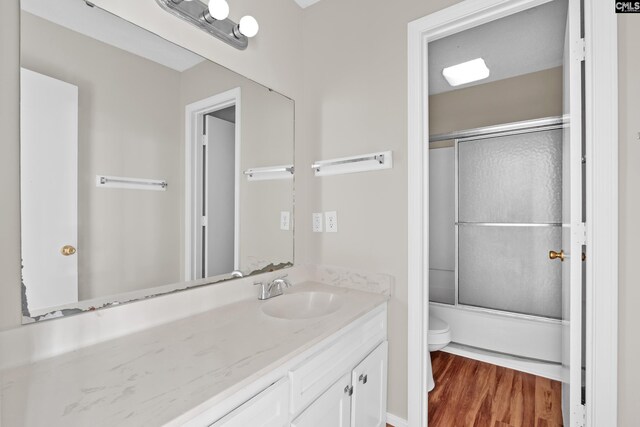 full bathroom featuring enclosed tub / shower combo, toilet, wood-type flooring, and vanity