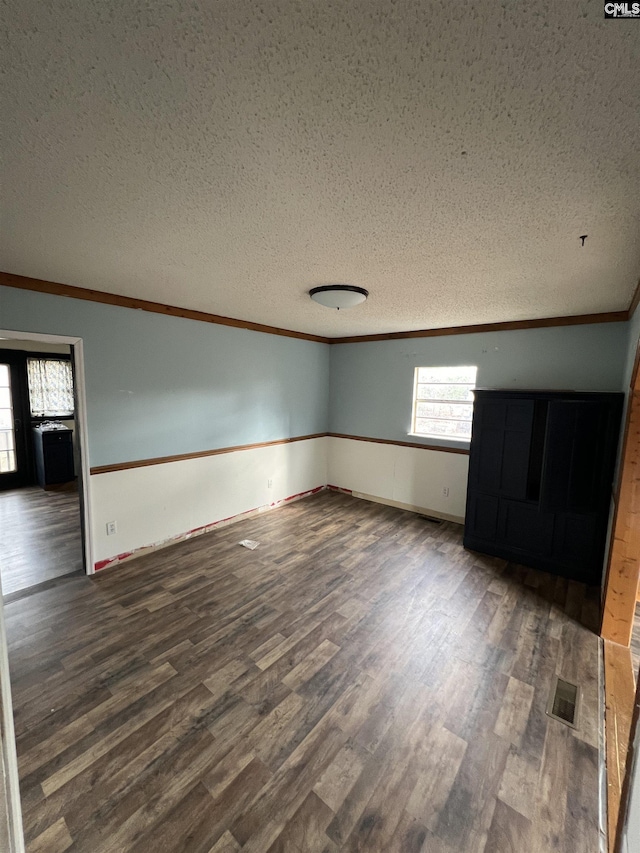 unfurnished room with a wealth of natural light, dark wood-type flooring, a textured ceiling, and ornamental molding