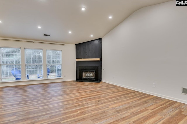 unfurnished living room with a large fireplace, lofted ceiling, and light wood-type flooring