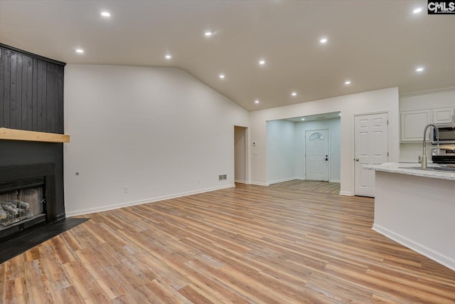 unfurnished living room featuring sink, a large fireplace, lofted ceiling, and light wood-type flooring