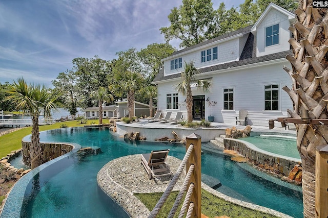 rear view of property with an infinity pool, roof with shingles, an outdoor structure, and a patio