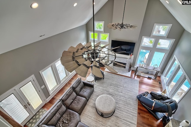 living area featuring a fireplace, visible vents, a ceiling fan, wood finished floors, and high vaulted ceiling