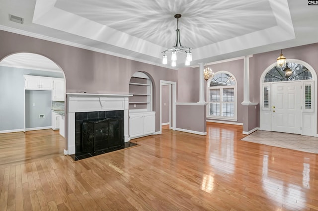 unfurnished living room with a raised ceiling, built in shelves, a tiled fireplace, and light wood-type flooring