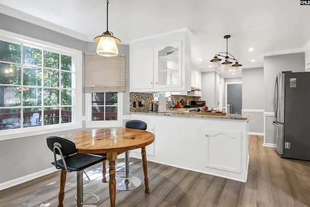 kitchen with stainless steel refrigerator, light stone countertops, kitchen peninsula, pendant lighting, and white cabinets