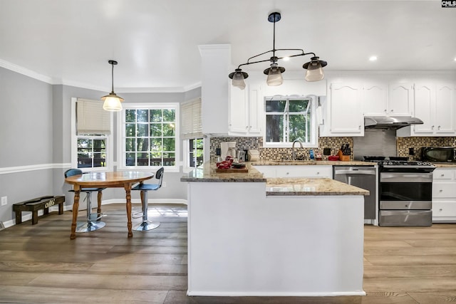 kitchen with stainless steel appliances, sink, pendant lighting, white cabinets, and light hardwood / wood-style floors