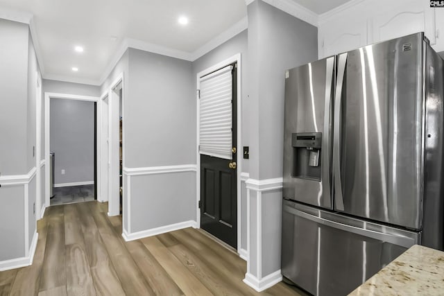 kitchen featuring crown molding, stainless steel fridge, light wood-type flooring, light stone counters, and white cabinetry