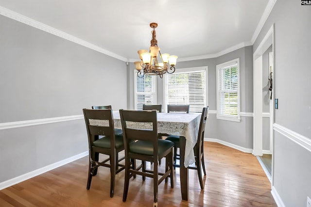 dining space featuring wood-type flooring, ornamental molding, and a notable chandelier