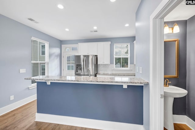 kitchen featuring white cabinets, light stone counters, tasteful backsplash, a kitchen bar, and stainless steel fridge with ice dispenser